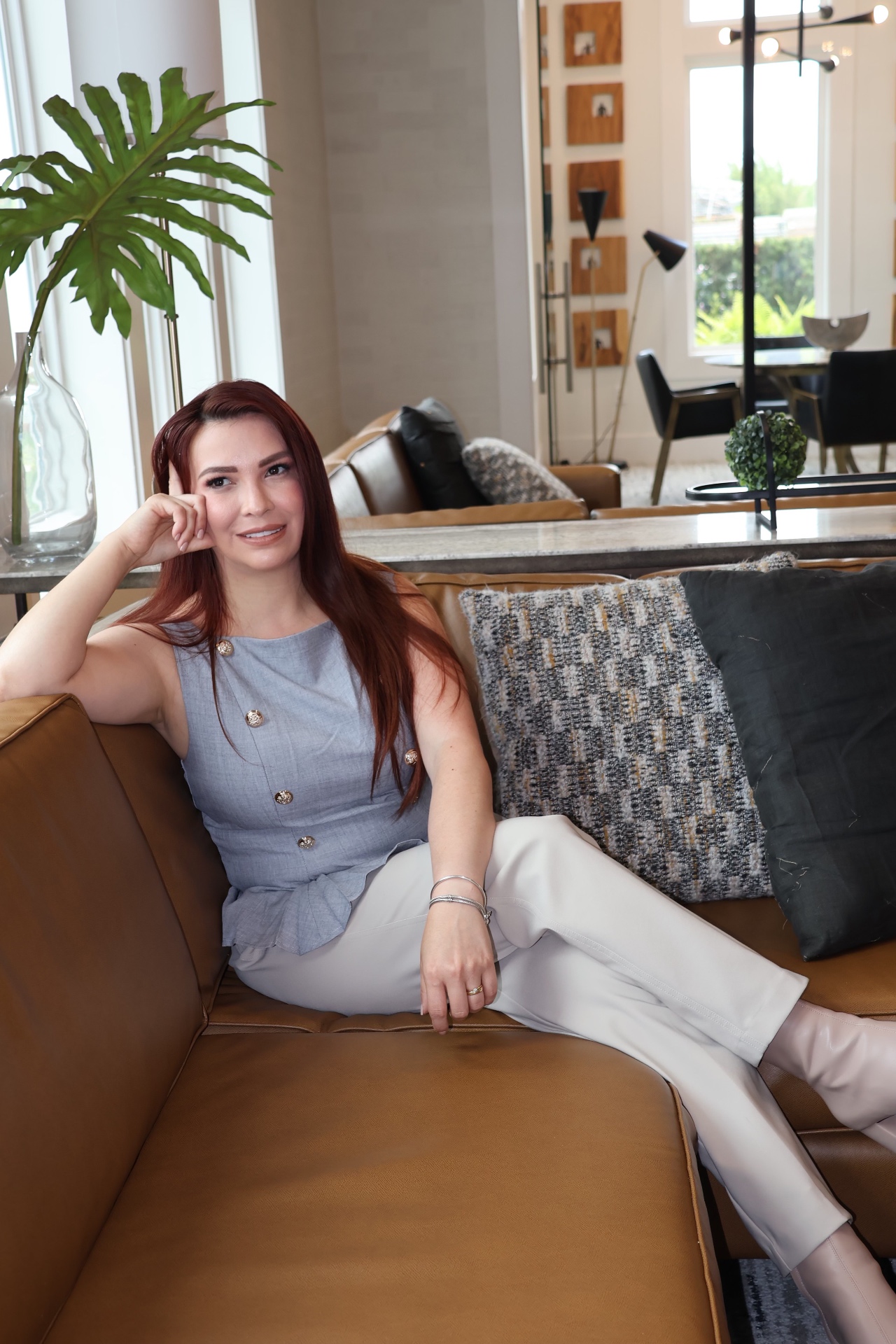 Angela Viloria, diseñadora de interiores en Orlando, FL, sentada en un sofá de cuero marrón en un interior moderno y luminoso